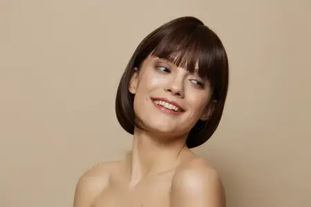 Женщина улыбается, демонстрируя уход за кожей и шарм, с короткой стрижкой на бежевом фоне