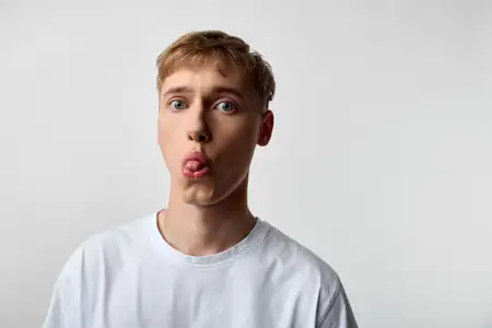 Игривый мужчина с высунутым языком, яркая студийная обстановка и чистый фон, энергичное настроение, непринужденная модная атмосфера, идеально подходит для развлекательных, молодежных и маркетинговых…