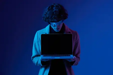 Портрет стильного хакера мужского пола с ноутбуком и футуристическими очками в синем свете