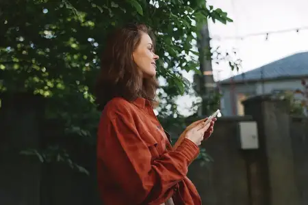 Яркая женщина на открытом воздухе, улыбается, смотрит в сторону, одета в уютный свитер, естественные цвета, фон — залитый солнцем сад, непринужденное и расслабленное настроение