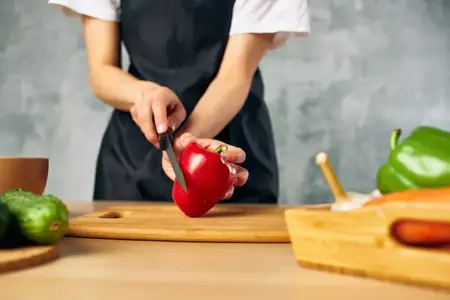 Женщина в черном фартуке на кухне нарезает овощи