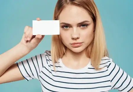 Женщина на синем фоне в полосатой футболке держит в руке визитную карточку