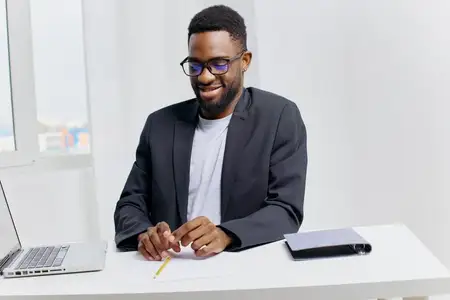 Молодой специалист, глубоко погружённый в работу, использует ноутбук и ручку, сосредоточенно работая в стильном современном офисе