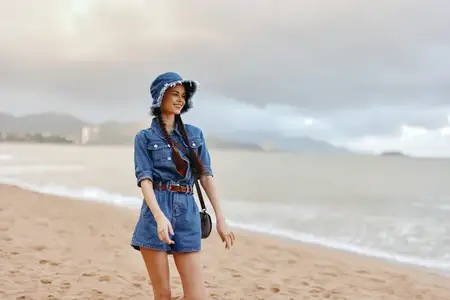 Спокойная красота: молодая привлекательная девушка в белой шляпе наслаждается солнечным летним отпуском на тропическом пляже, глядя на океан с расслабленным и счастливым выражением лица