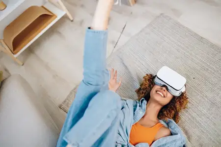 Весёлое время с виртуальной реальностью: улыбающаяся женщина в VR-очках наслаждается футуристическим игровым опытом, сидя на диване дома