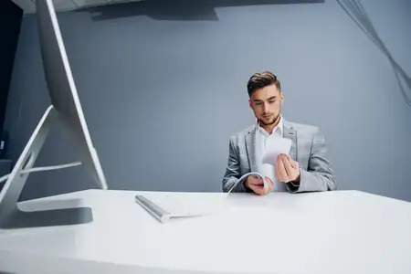 Красивый мужчина работает за компьютером в офисе и разбрасывает документы