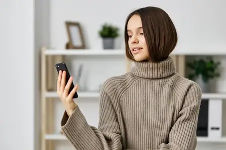 Молодая женщина сидит дома на диване, делает селфи на смартфон