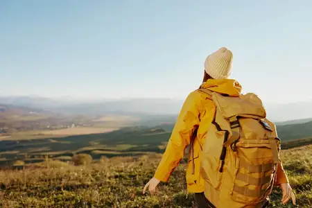 Путешественница в жёлтой куртке и шляпе с рюкзаком отдыхает в горах