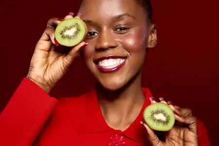 Крупный план счастливой темнокожей женщины с яркой улыбкой, держащей половинки зелёного киви
