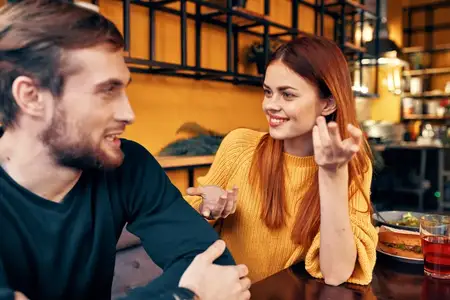 Мужчина и женщина сидят в кафе за столом и жестикулируют руками, друзья, эмоции, веселье, интерьер