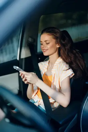 Молодая женщина сидит в машине и печатает сообщение на смартфоне
