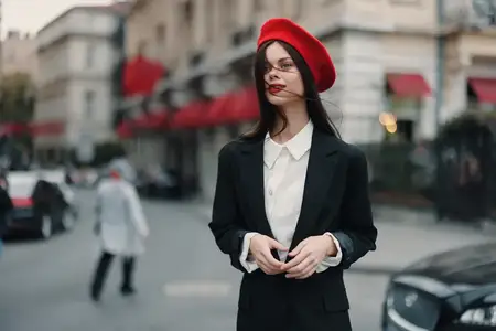 Модный портрет женщины: она улыбается, показывая зубы, стоит на улице на фоне города в стильной одежде, с красными губами и красным беретом