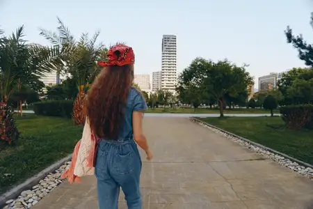 Женщина в стиле лайфстайл, одетая в современный деним в стиле бохо-вестерн, идёт по мощёной дорожке в окружении деревьев и городских зданий, снятая в тёплом, ностальгическом плёночном цвете