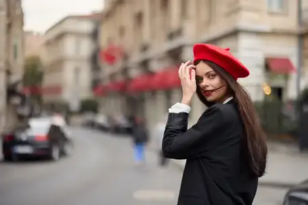 Портрет модной женщины, которая улыбается, обнажая зубы, и стоит на улице на фоне города
