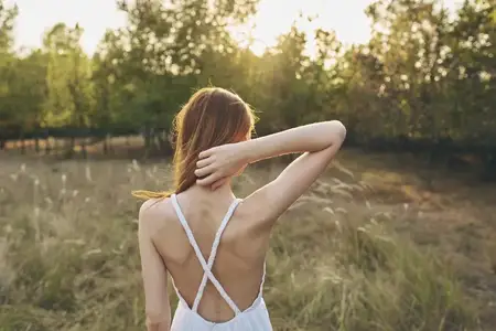 Женщина на лугу среди природы, рядом с летними деревьями, отдыхает на солнце