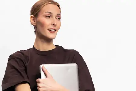 Улыбающаяся женщина прижимает ноутбук к груди, на ней темная футболка