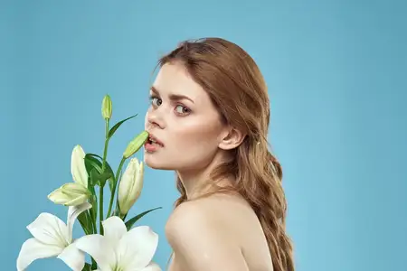 Женщина с букетом белых цветов на синем фоне, обнаженные плечи, красивое лицо