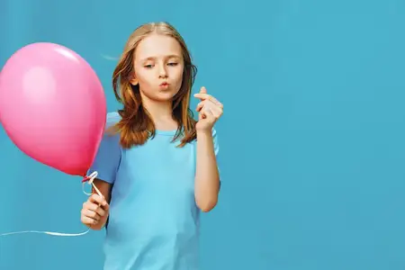 Веселая девочка с розовым воздушным шаром, передающая ощущение юности и счастья на фоне ярко-голубого задника, идеально подходит для концепций, связанных с детством и радостью