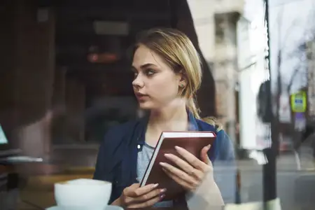 Деловая женщина с книгой в руках и чашкой кофе в кафе, ведущая активный образ жизни