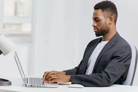 Сосредоточенный профессионал в костюме усердно работает за ноутбуком за стильным офисным столом, олицетворяя продуктивность и концентрацию