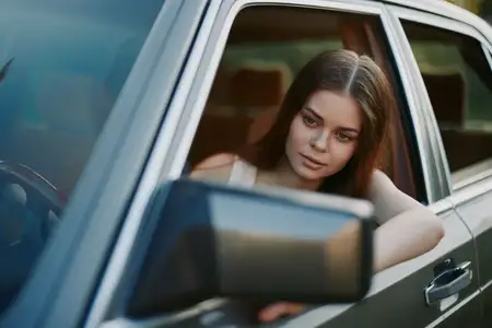 Молодая женщина с длинными волосами смотрит из окна автомобиля, воплощая безмятежность и красоту