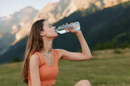 Сцена на открытом воздухе: подтянутая женщина пьет воду на фоне холмов и далеких гор