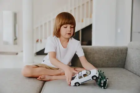 Маленький мальчик увлеченно играет с разноцветными игрушечными машинками, наслаждаясь моментом творчества и воображения в уютной гостиной, залитой естественным светом