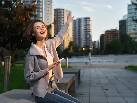 Весёлый человек стоит в городском парке, улыбаясь и печатая на смартфоне