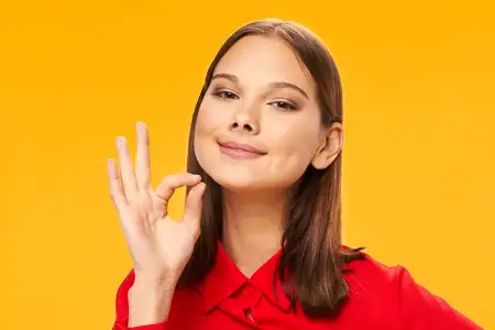Красивая женщина в красной рубашке жестикулирует руками на жёлтом фоне