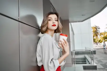 Женщина в красной юбке с чашкой кофе позирует на улице возле здания