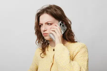 Взволнованная молодая женщина в желтом трикотаже прижимает смартфон к уху