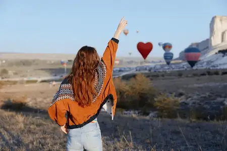 Женщина с длинными рыжими волосами взволнованно указывает на красочный воздушный шар в небе