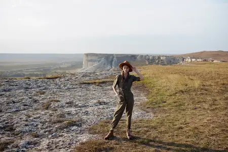 Женщина в шляпе стоит на холме, наслаждаясь красивыми пейзажами во время летнего туристического приключения