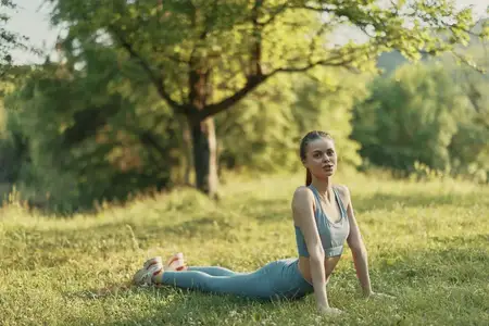 Стройная молодая женщина занимается йогой на открытом воздухе в солнечный день в окружении природы, демонстрируя концепцию здорового образа жизни, безмятежность и физическую форму