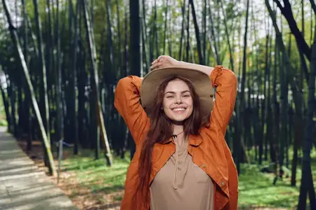 Женщина улыбается, на ней шляпа, она в лесу