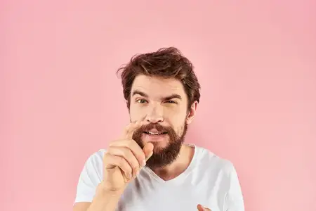 Крупный план бородатого мужчины в белой футболке, который жестикулирует руками на розовом фоне