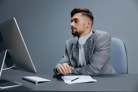 Красивый мужчина работает за компьютером в наушниках в офисе на изолированном фоне