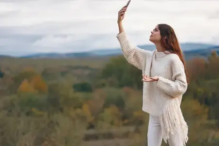 Женщина в горах: улыбающаяся любительница приключений в походе, делающая селфи на мобильный телефон на фоне прекрасного природного пейзажа