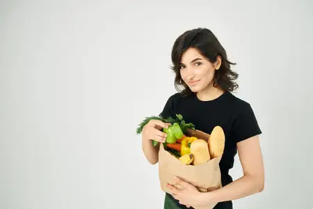 В руке человека находится пакет с продуктами, наполненный овощами, что символизирует доставку здоровой пищи