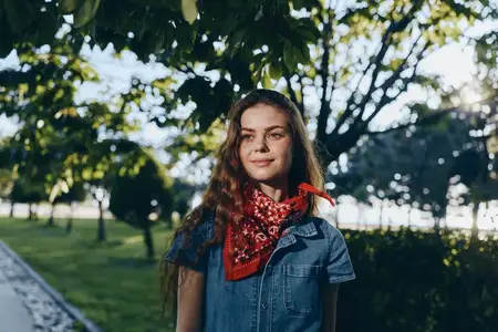 Женщина в стиле бохо-вестерн, одетая в джинсовую уличную одежду, с красной банданой, наслаждается теплым естественным светом на улице в окружении деревьев и зелени