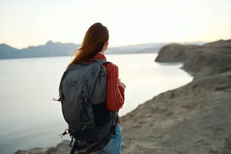 Путешествия, туризм: молодая женщина с рюкзаком у моря в горах на природе