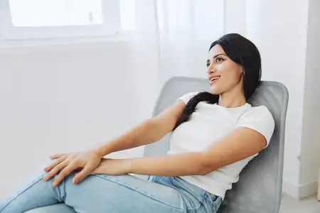 Женщина слушает музыку в наушниках, сидя дома на стуле