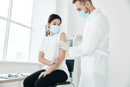 Врач в медицинском халате и маске делает инъекцию в плечо пациентке
