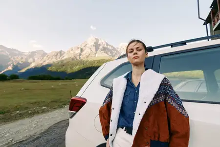 Женщина позирует, опираясь на машину у гор