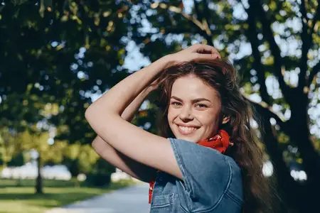Улыбающаяся женщина в стиле casual, одетая в современный бохо-вестерн деним стритстайл, наслаждается солнечным днем на улице, демонстрируя расслабленную повседневную моду в теплых тонах плёночного…
