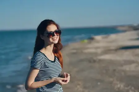 Путешественница в солнцезащитных очках и футболке отдыхает на пляже у моря в горах