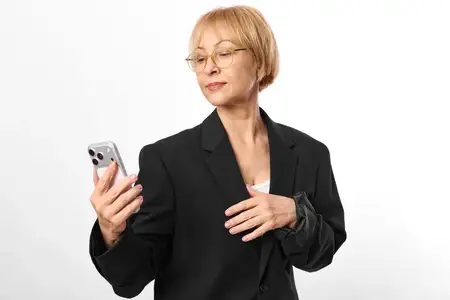 Женщина в деловом костюме держит смартфон для общения, зрелый профессионал в очках