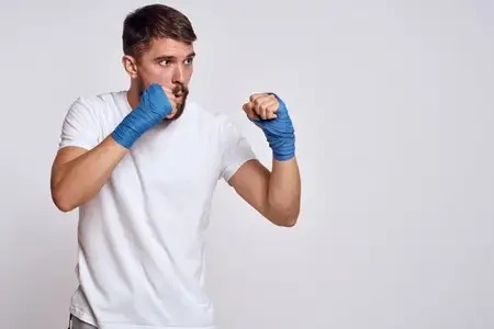 Спортивный мужчина в белой футболке, синие боксёрские бинты на руках, тренировочные упражнения