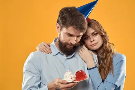 Мужчина и женщина веселятся на праздновании дня рождения на жёлтом фоне, на них колпаки