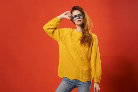 Женщина в желтом свитере и синих очках позирует для фото